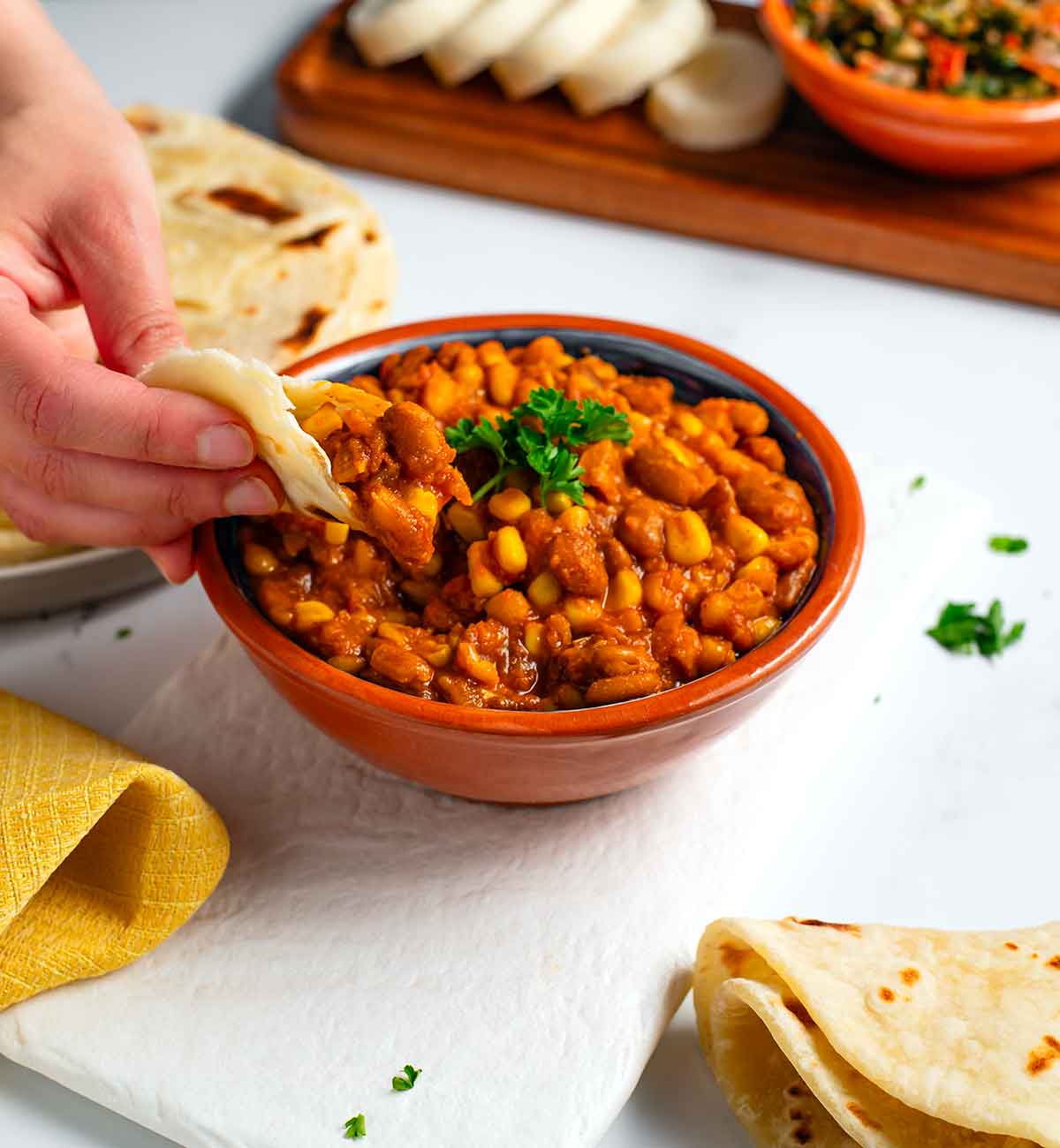 A hand scoops githeri from a small bowl with soft Kenyan chapati.