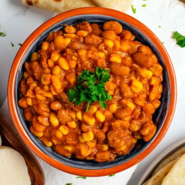 Top down view of githeri, a Kenyan bean and rice stew. This version has a thick tomato gravy and uses pinto beans and white navy beans. The githeri is garnished with fresh parsley