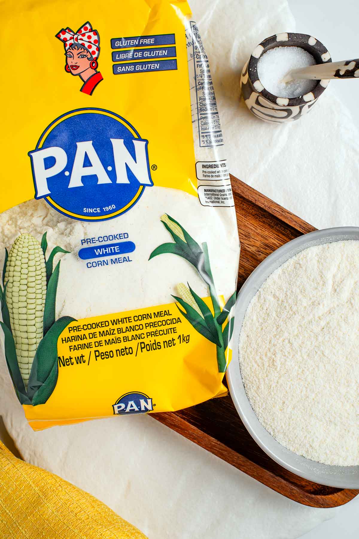 Top down view of a package of fine white cornmeal. A small bowl filled with the cornmeal rests beside the package. The cornmeal in the bowl is bright white and very fine.