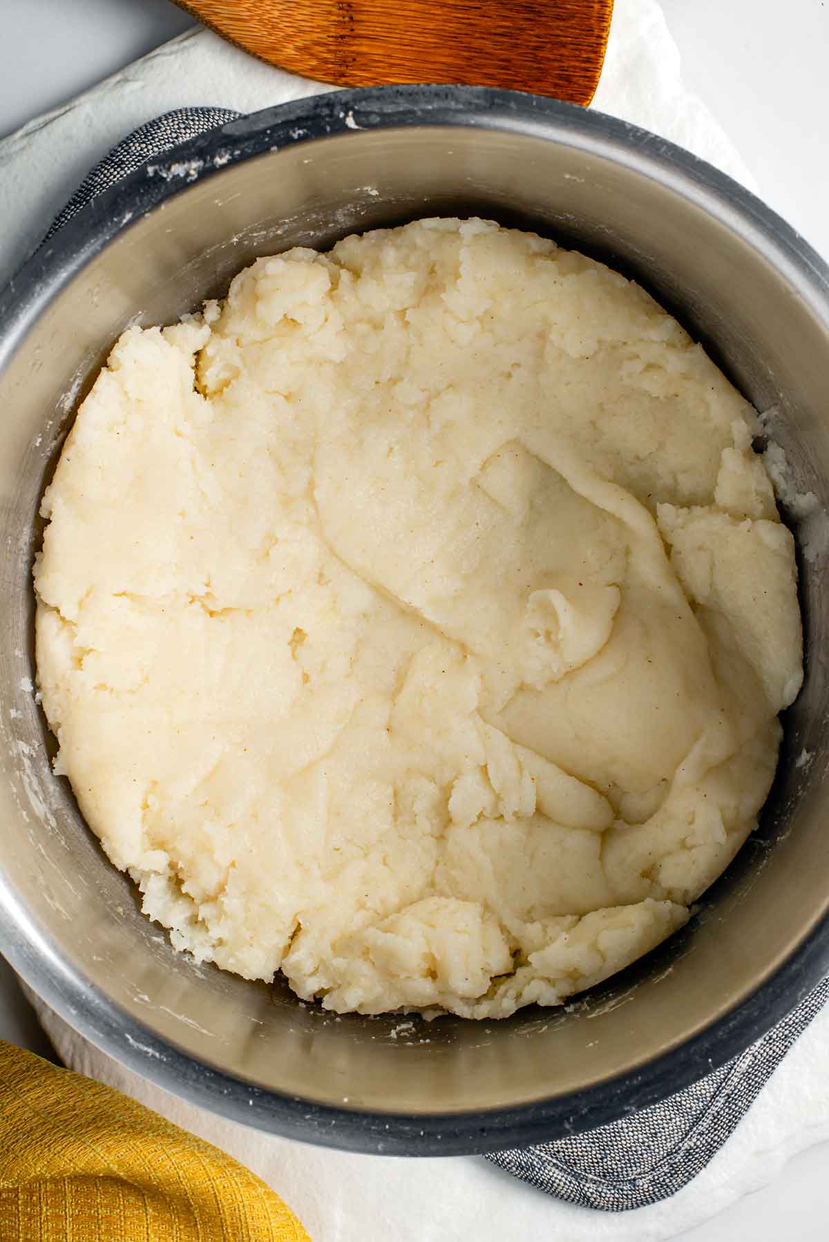 Top down view of cooked ugali in a metal pot. The ugali is pressed into a single layer. It is clump free but has some texture from being prodded with a spoon.