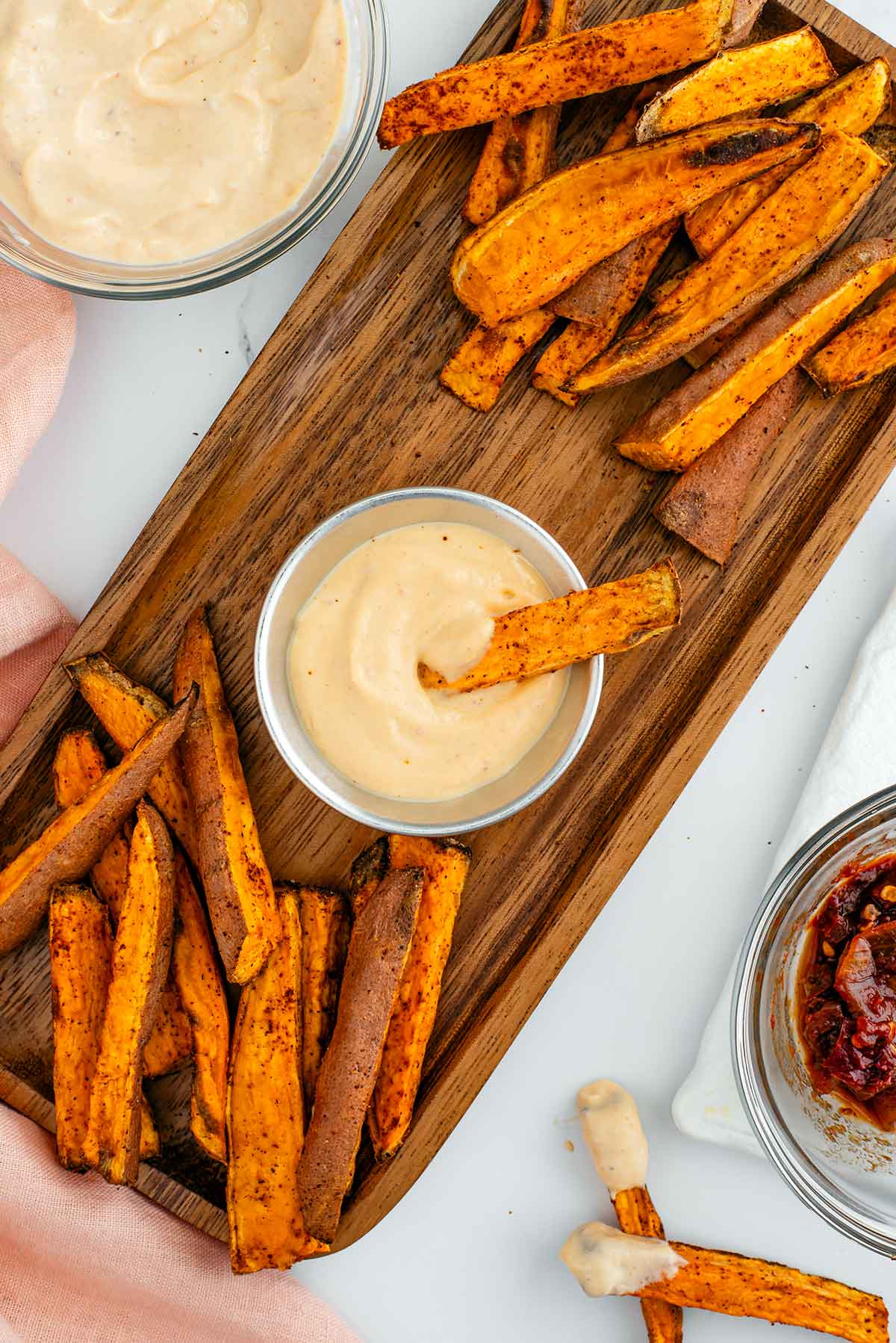 Top down view of oil-free chipotle mayo in a small tin. A sweet potato fry rests in the thick, creamy, and speckled mayo. More sweet potato fries rest on a wooden tray around the mayonnaise.