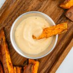 Top down view of oil-free chipotle mayo in a small tin. A sweet potato fry rests in the thick, creamy, and speckled mayo.