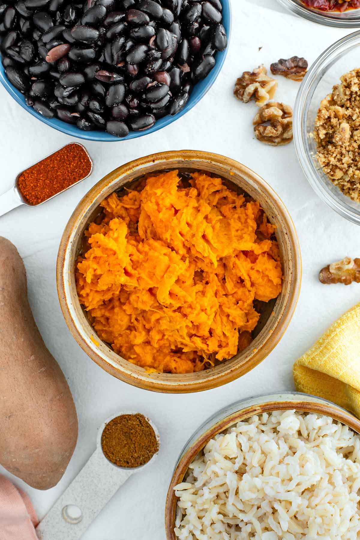 Top down view of ingredients. Mashed sweet potato, black beans, cooked rice, walnuts, and seasonings.