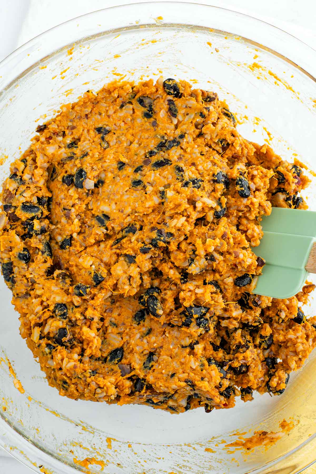 Top down view of the burger patty ingredients mashed in a glass bowl. The sweet potato and rice are well mashed but the black beans are still mainly intact.
