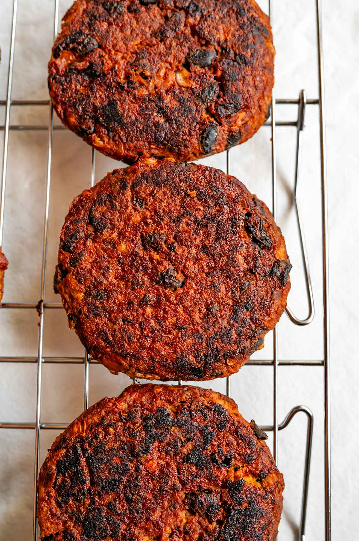 Top down view of cooked sweet potato black bean burgers. The chipotle BBQ sauce gives the burgers a deep red colour reminiscent of the colour of meat. The burgers also have a nice bit of charring from the flat griddle.