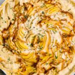 Close up view of dairy free scalloped potatoes. They are incredibly creamy with golden edges and the potatoes are arranged in a spiral pattern. Caramelized strands of onion can be seen on top of the potatoes and the dish is garnished with chopped rosemary.