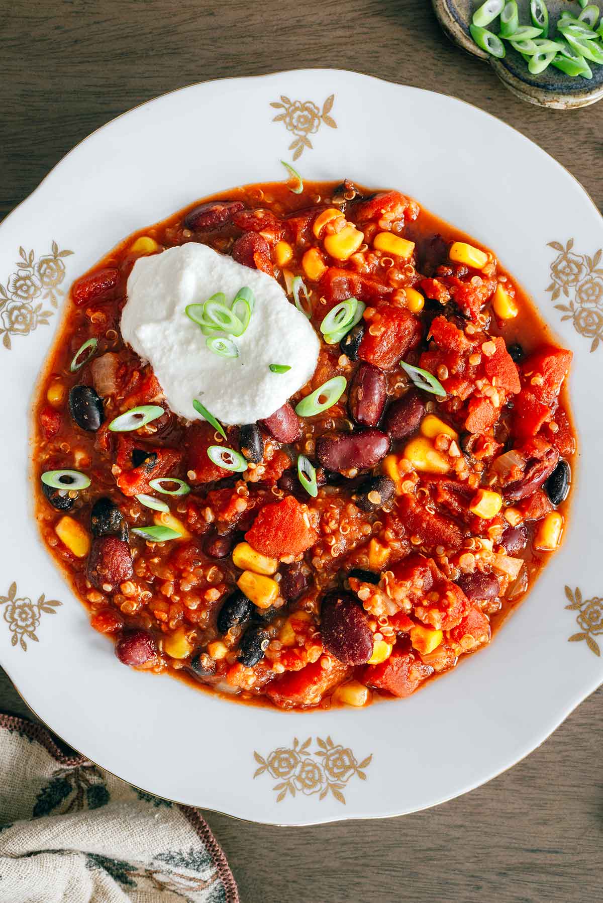 Top down view of quinoa chili in a vintage bowl. The chili is thick but not too thick and garnished with a creamy dollop of vegan sour cream and sliced green onion.