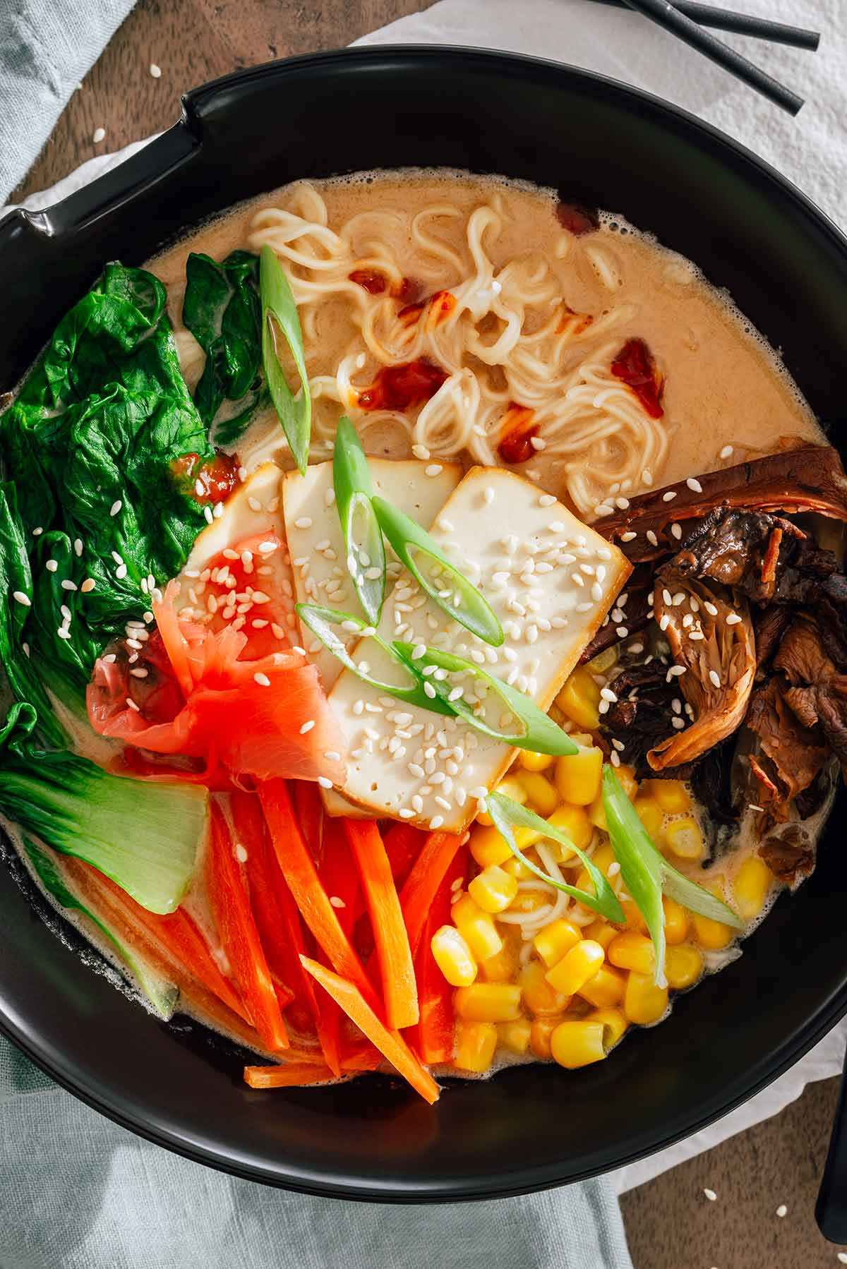 Top down view of a homemade peanut butter ramen. The broth is creamy, the toppings are brightly coloured, and small drips of chili paste are dotted throughout the broth.