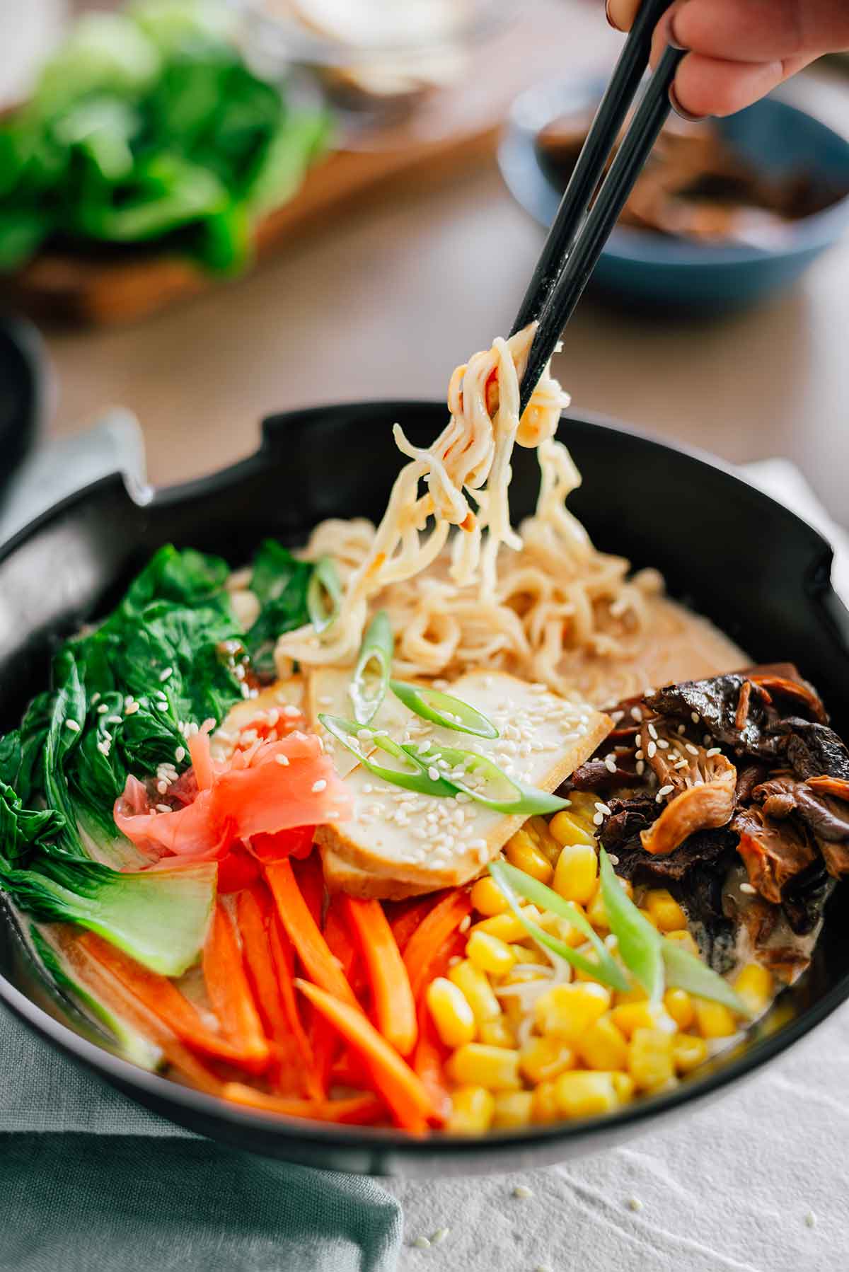 Side view of chopsticks pulling ramen noodles up from a colourful bowl of creamy peanut butter ramen.