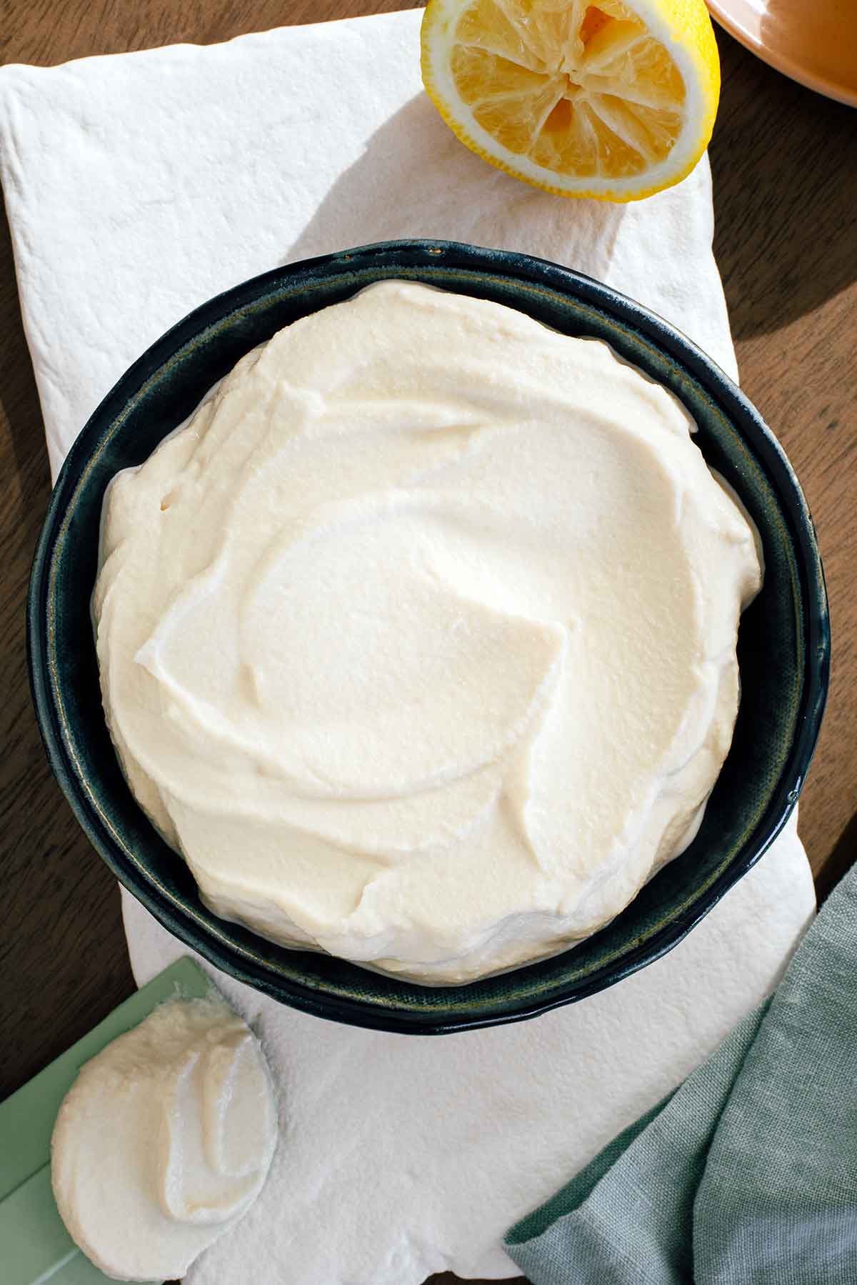 Top down view of a bowl of creamy whipped tofu. The tofu is fluffy and light. Swirls from a silicone spatula are clearly visible in the creamy tofu and the spatula rests next to the bowl.