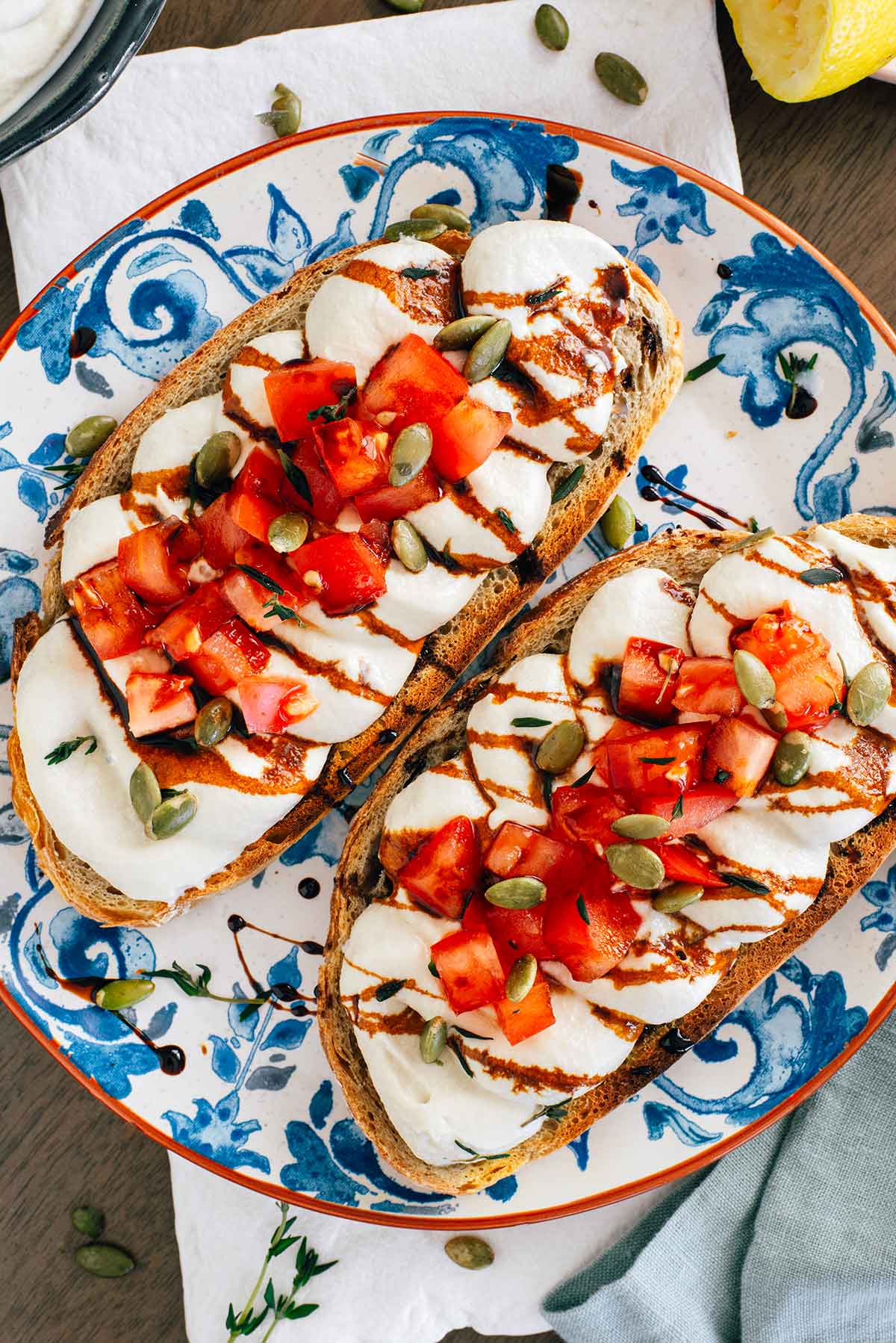 Top down view of two slices of loaded toast. The toast is topped with fluffy whipped tofu and then garnished with diced tomato, pumpkin seeds, fresh thyme and a balsamic reduction.