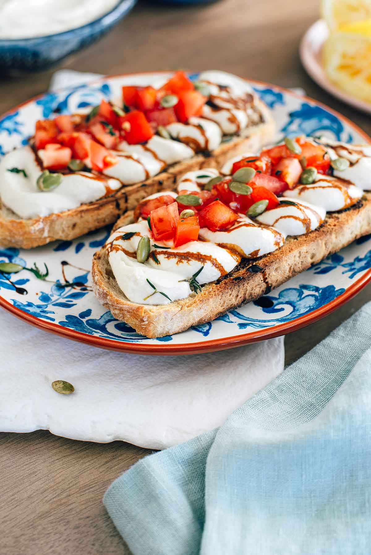 Side view of fluffy whipped tofu on a slice of toast. The pillowy tofu is garnished with diced tomato, pumpkin seeds, fresh thyme, and a balsamic reduction.