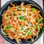 Top down view of a colourful cabbage salad in a small bowl. Green cabbage and carrot are shredded and mixed with bright green edamame and cilantro leaves. A peanut dressing lightly coats the salad which is topped with chopped roasted peanuts.
