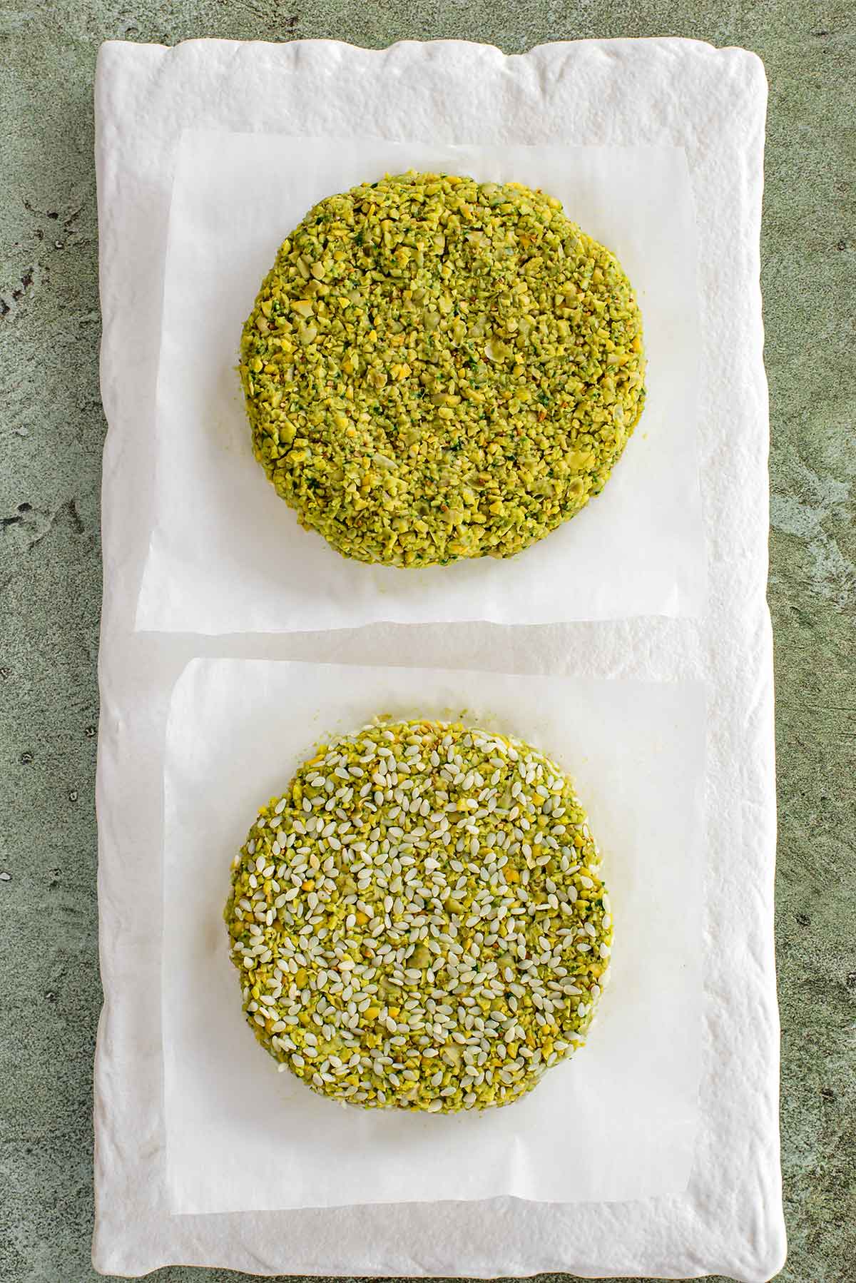 Top down view of falafel burger patties before being cooked. One patty is coated in raw sesame seeds.