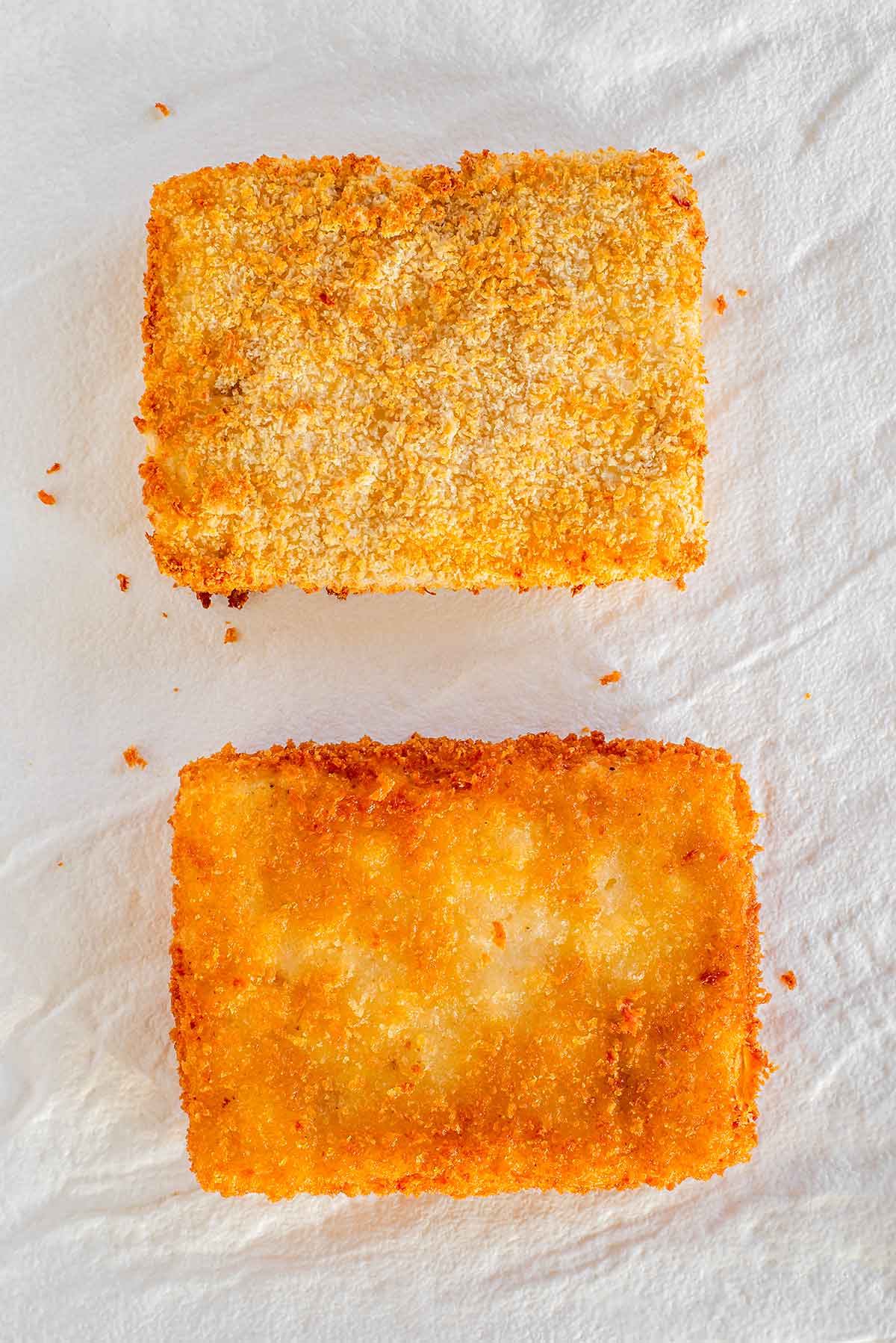 Top down view of two slices of tofu katsu. One has been air fried and is golden and crispy but not as saturated and evenly fried as the other slice which was deep fried.