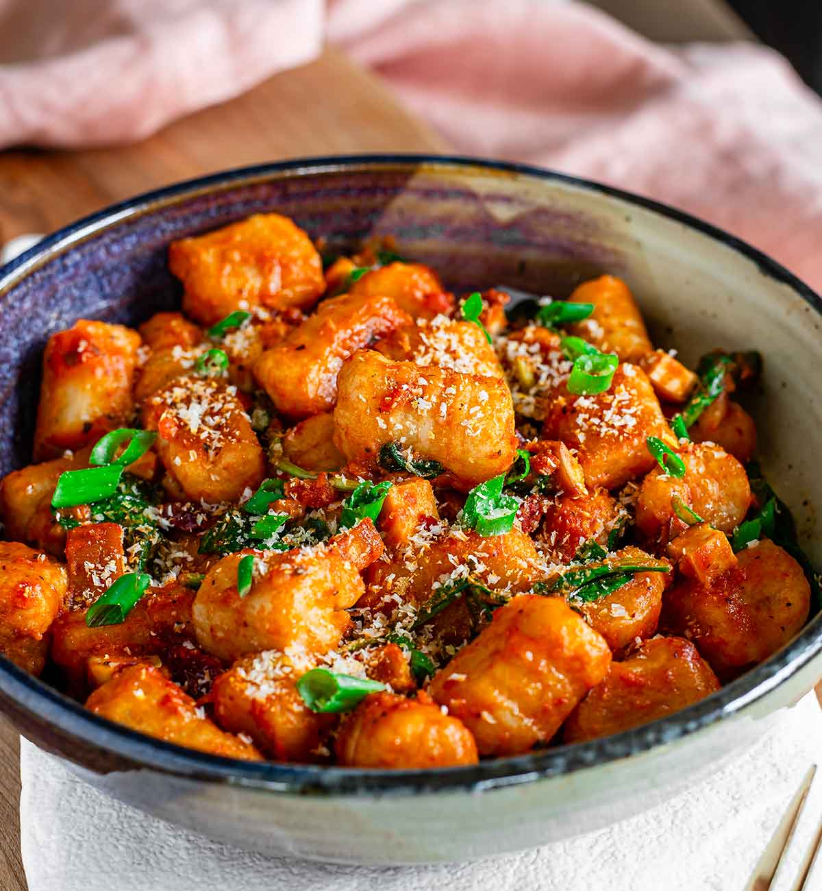 Side view of a bowl of gnocchi covered in tomato sauce with sun-dried tomatoes, smoked tofu, spinach, green onion, and vegan parmesan. The gnocchi is soft, fluffy, and grooved.