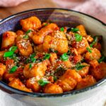 Close up side view of fluffy gnocchi made from leftover mashed potatoes. The gnocchi is ribbed and covered in a creamy tomato sauce with sun-dried tomatoes, smoked tofu, spinach, green onion, and vegan parmesan cheese.
