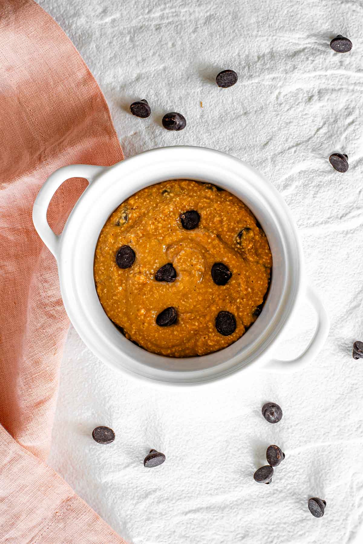 Top down view of vegan deep dish cookie batter in a mini casserole dish before it has been baked. The batter is thick but has a more gooey texture than a traditional cookie dough.