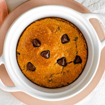 Top down view of a vegan deep dish cookie in a mini casserole dish. The cookie is golden brown, speckled with chocolate chips, and has a crispy edge that has pulled away from the baking dish.