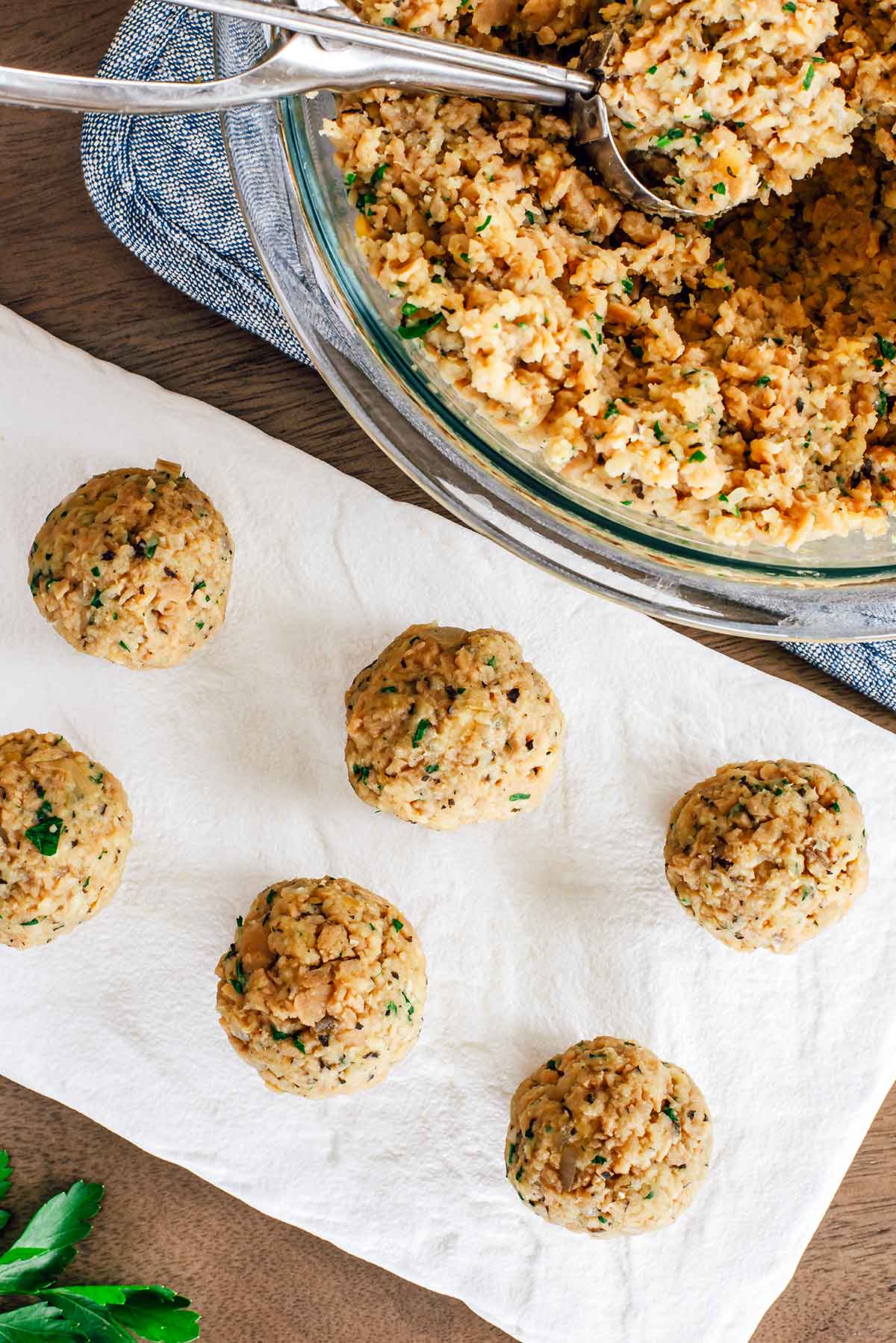 Top down view of a vegan meatball mixture being formed into individual meatballs. The balls are 1.5 inches thick and speckled with fresh parsley.