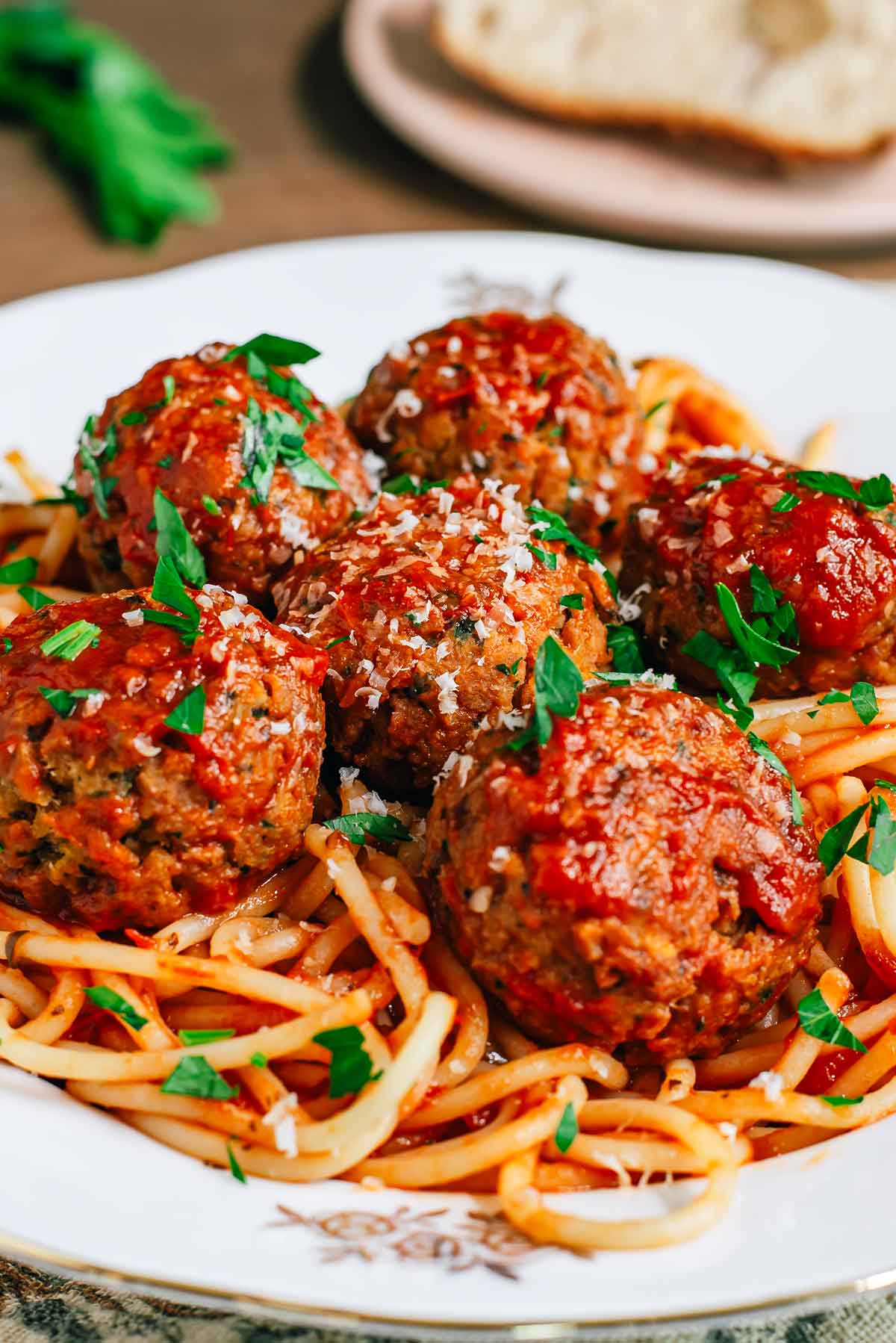 Side view of juicy vegan meatballs atop a bed of spaghetti. The succulent looking meatballs are covered in tomato sauce and sprinkled with fresh parsley and vegan parmesan cheese.