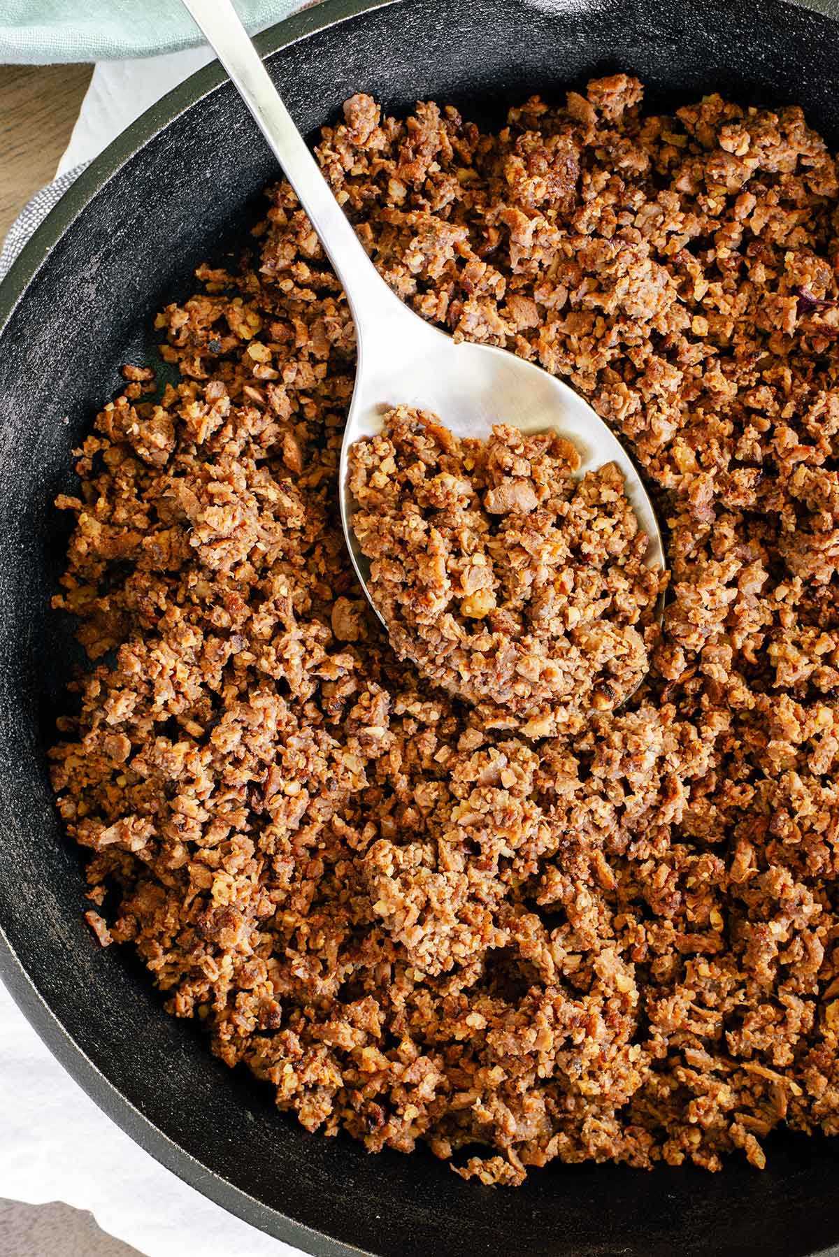 Top down view of cooked TVP taco meat in a cast iron frying pan. The "meat" is nicely browned and crumbly. A silver spoon rests in the mixture.