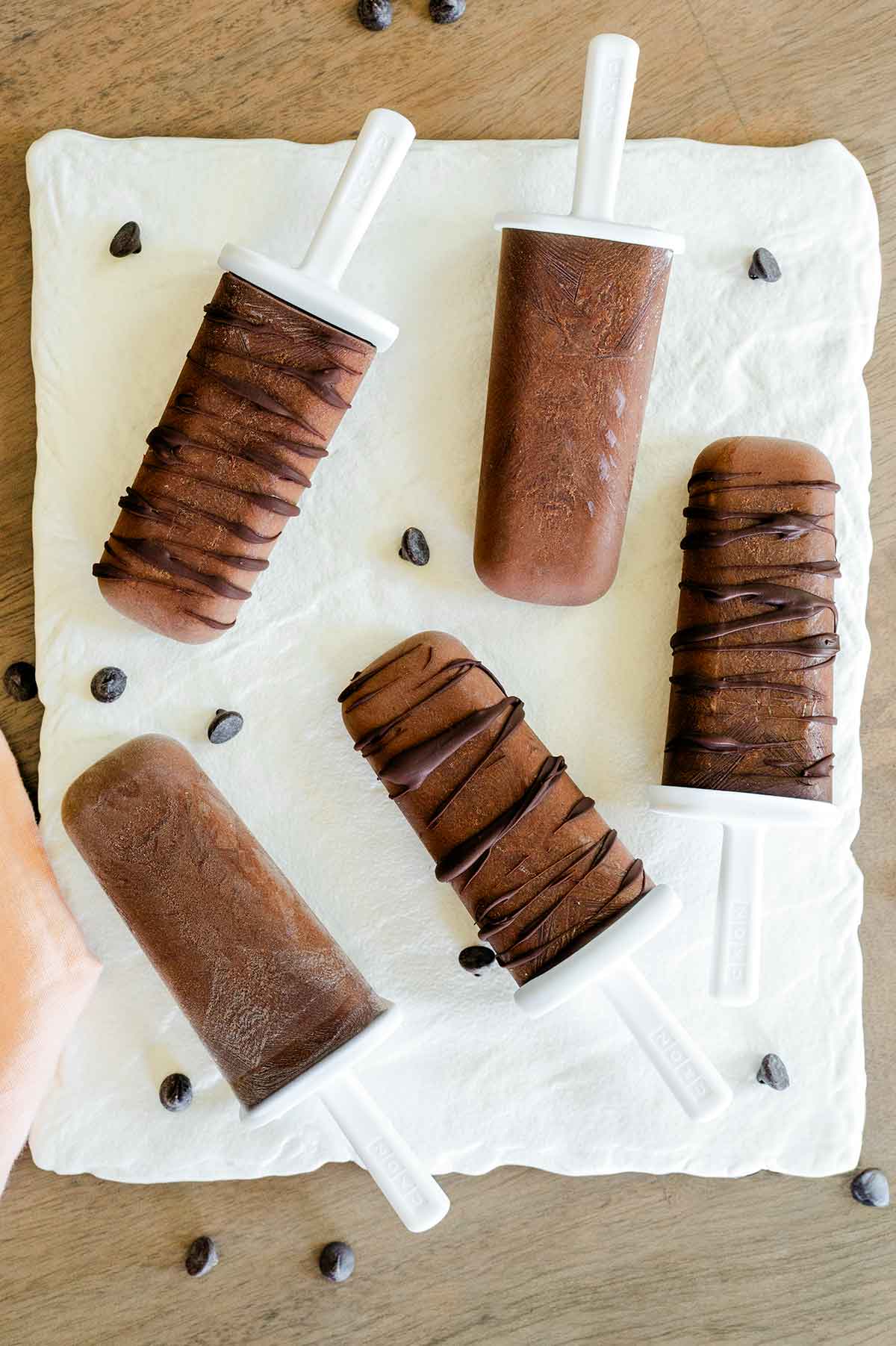 Top down view of vegan fudgsicles on a white tray. Some of the fudge pops are drizzled with dark chocolate.