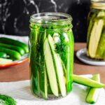 Side view of a quart jar filled with cucumber spears. The cucumber sits in a vinegar brine and is flavoured with garlic cloves, black peppercorns, and fresh dill.