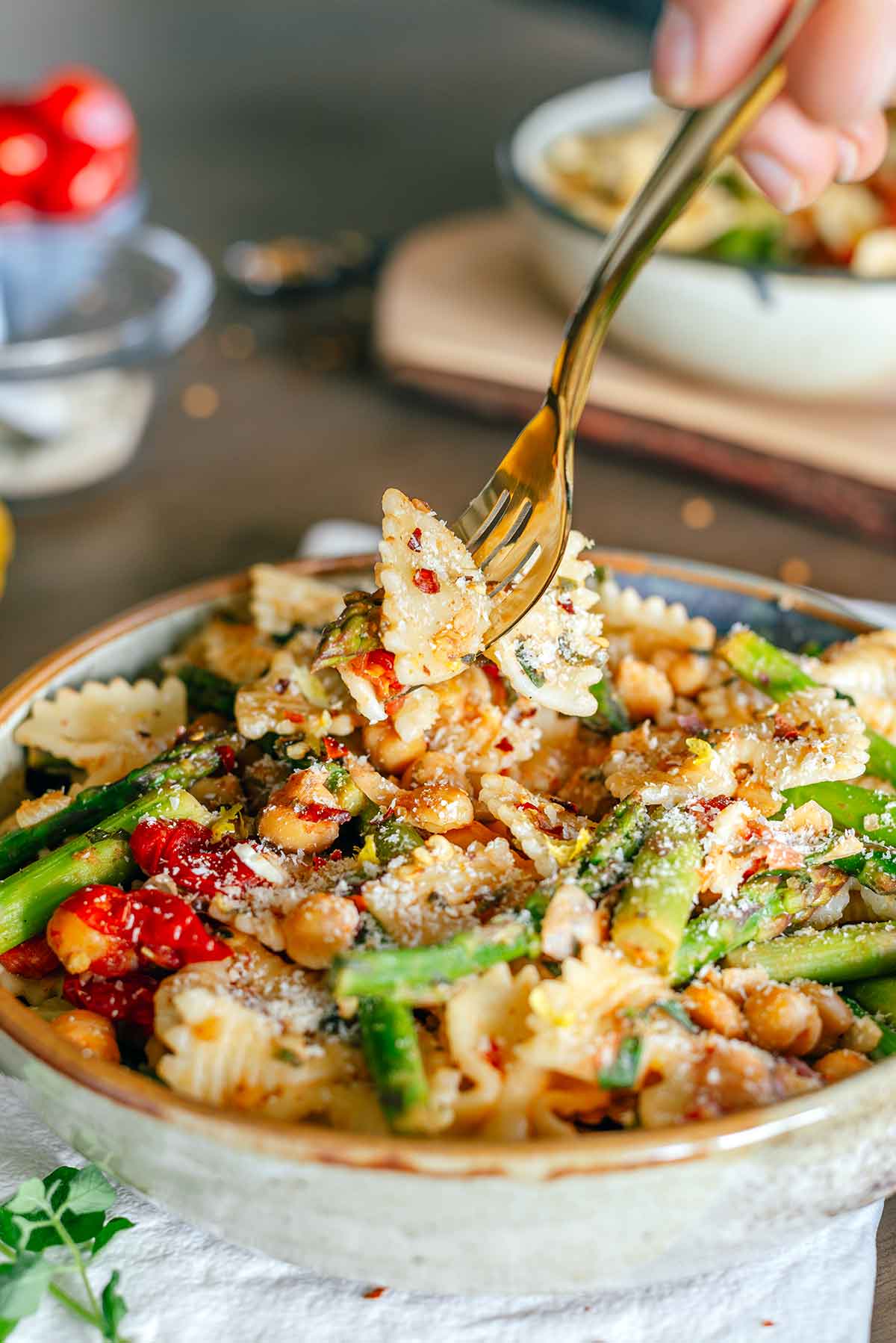 Side view of a hand holding a forkful of pasta above the lemon asparagus pasta dish. 