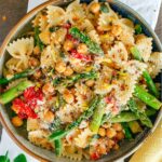 Top down view of a bow tie pasta dish with asparagus, grape tomatoes and chickpeas. A light clear lemony dressing with chili flakes, garlic, and herbs, coats the dish.