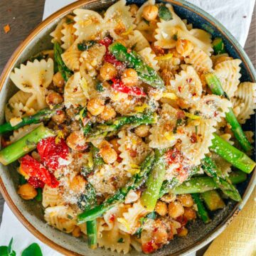 Top down view of a bow tie pasta dish with asparagus, grape tomatoes and chickpeas. A light clear lemony dressing with chili flakes, garlic, and herbs, coats the dish.