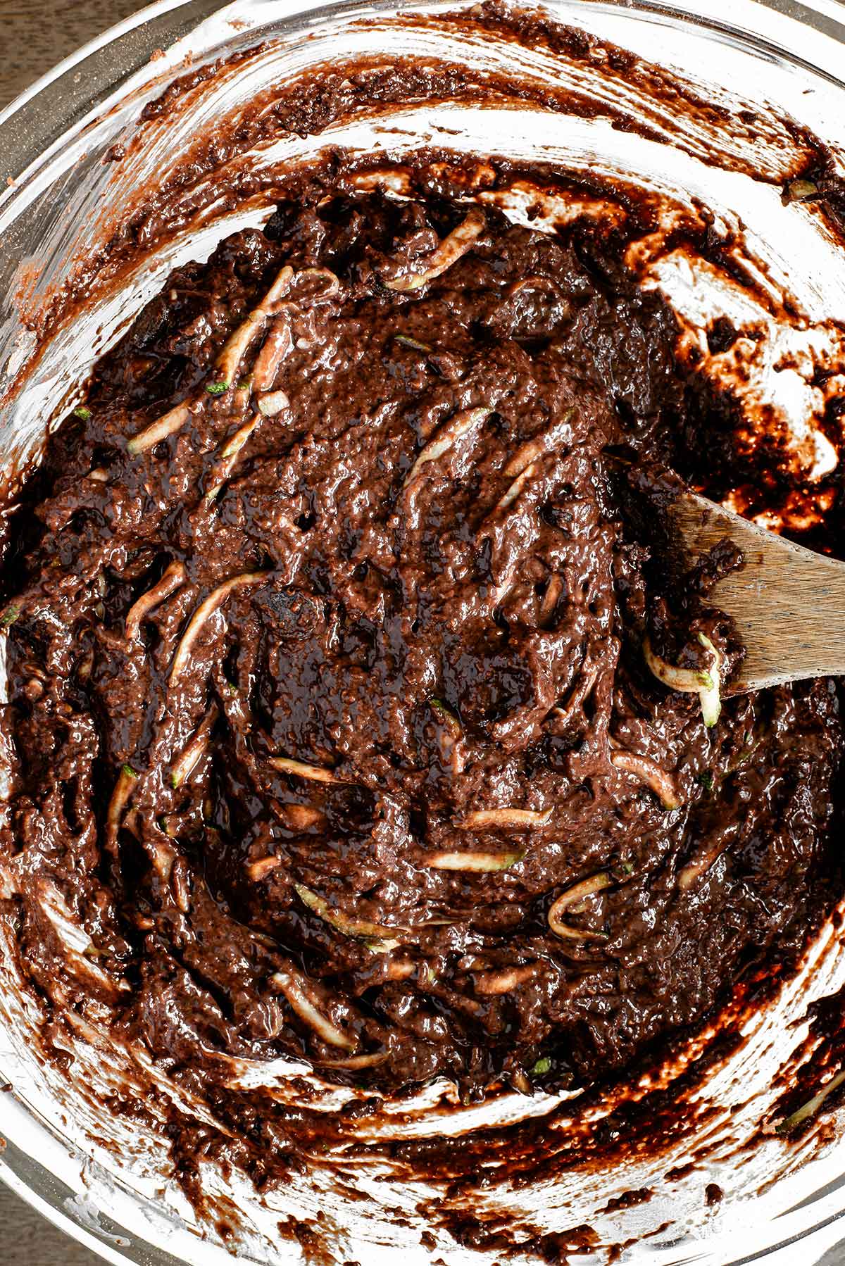 Top down view of the combined batter. Strands of shredded zucchini can be seen throughout the dark brown chocolate batter. The batter is moist but a scoopable texture; not pourable.