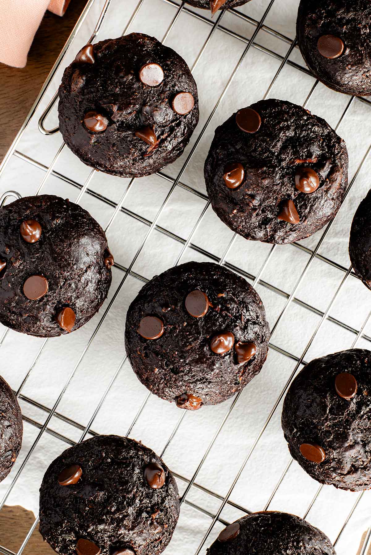 Top down view of vegan chocolate zucchini muffins on a wire cooling rack. The muffins are deeply chocolatey, speckled with chocolate chips, and have a nice shine on top.