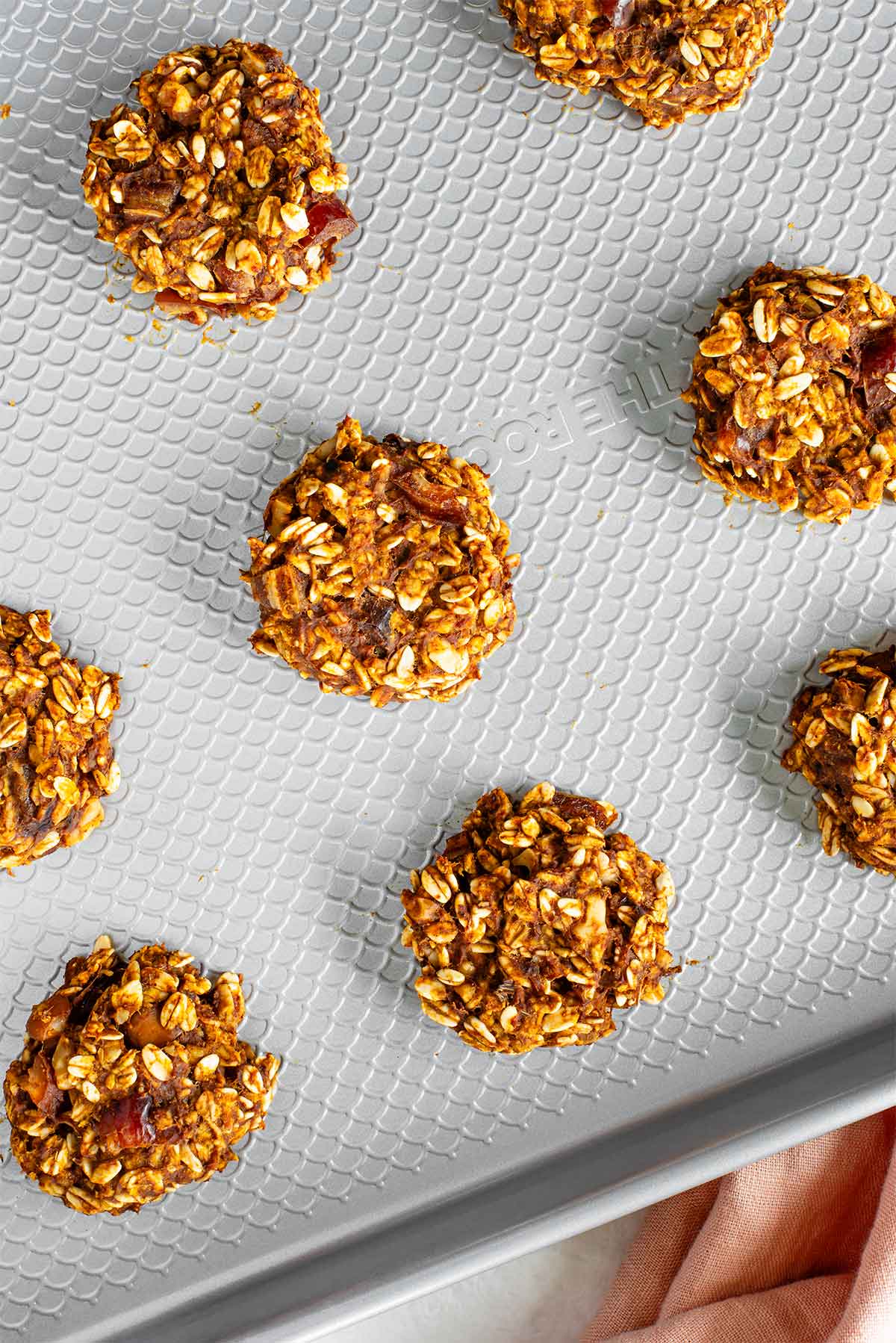Top down view of small pumpkin oat cookies on a cookie sheet after being baked. The cookies are firm and set.