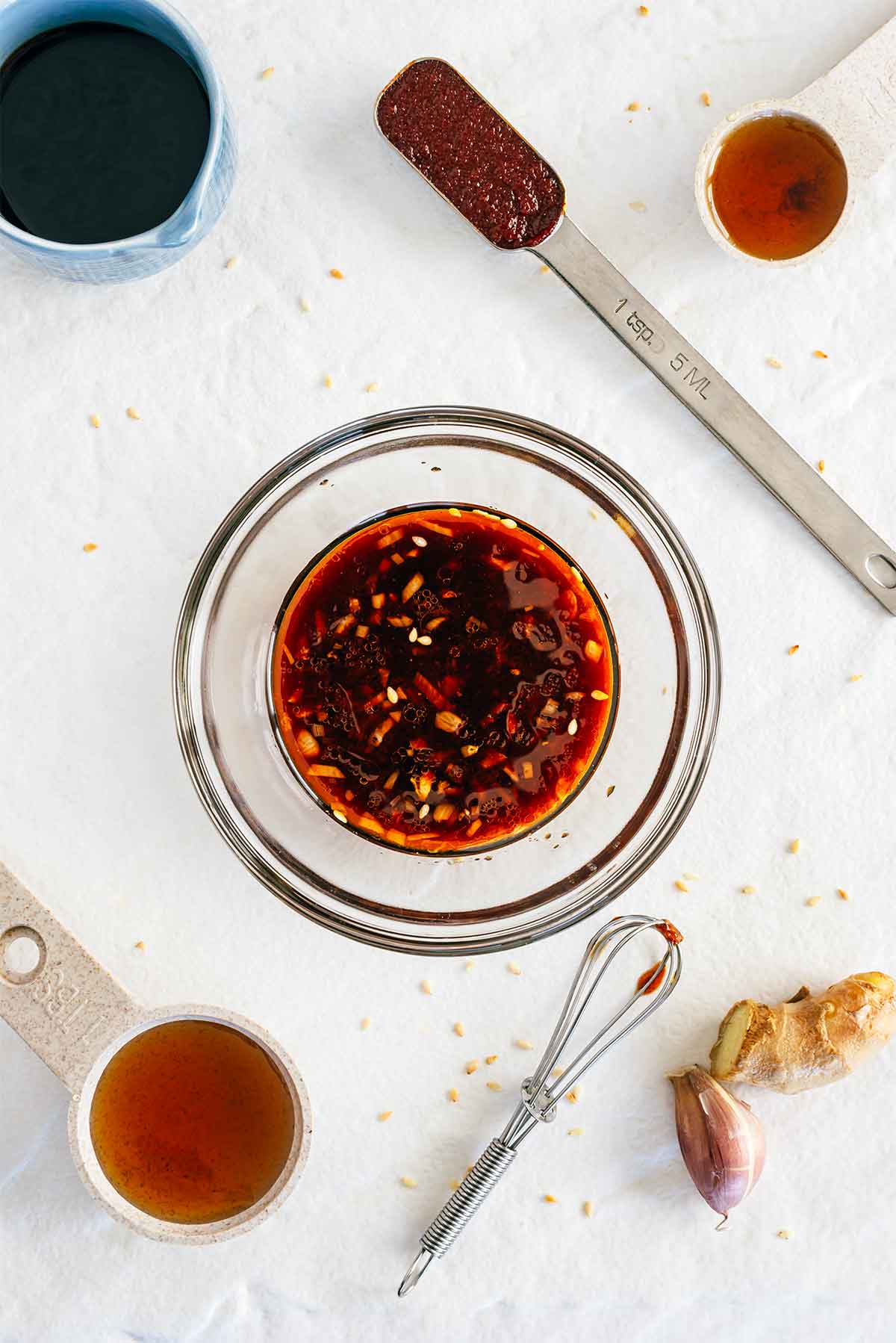 Top down view of the sauce combined in a small glass bowl. Surrounding the bowl are the individual ingredients. Soy sauce, gochujang, sesame oil, maple syrup, garlic, and ginger.