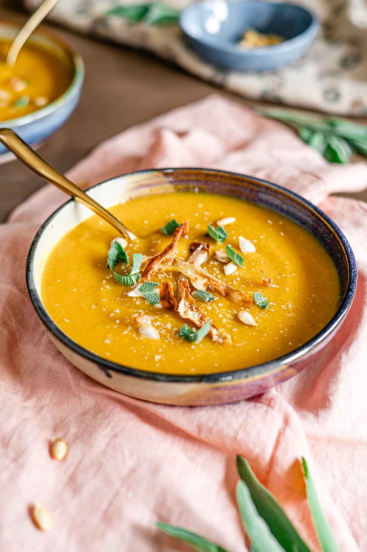 Side view of a thick and creamy butternut squash red lentil soup in a bowl. The soup is topped with sage, roasted squash peel and squash seeds.