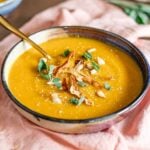 Side view of a thick and creamy butternut squash red lentil soup in a bowl garnished with roasted squash skin and seeds.