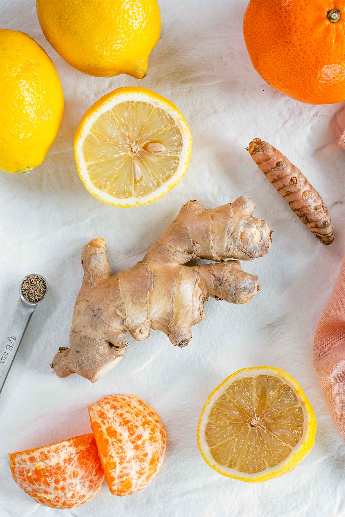Top down view of ingredients on a white tray. Shown are ginger root, turmeric root, lemons, oranges, and black pepper.